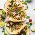 Overhead view of foul fish tacos in a row, next to lots of cilantro and lime slices