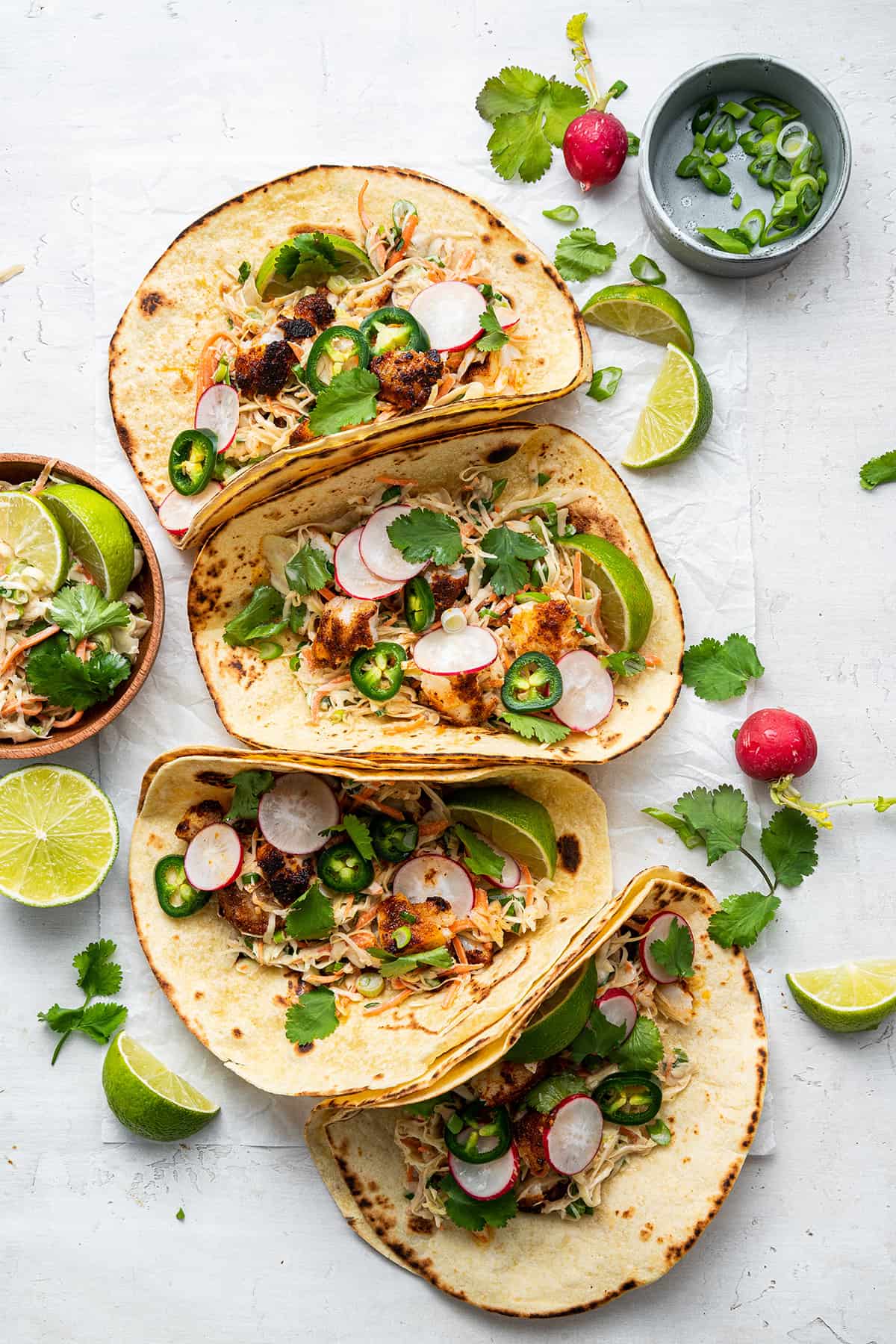 Overhead view of foul fish tacos in a row, next to lots of cilantro and lime slices