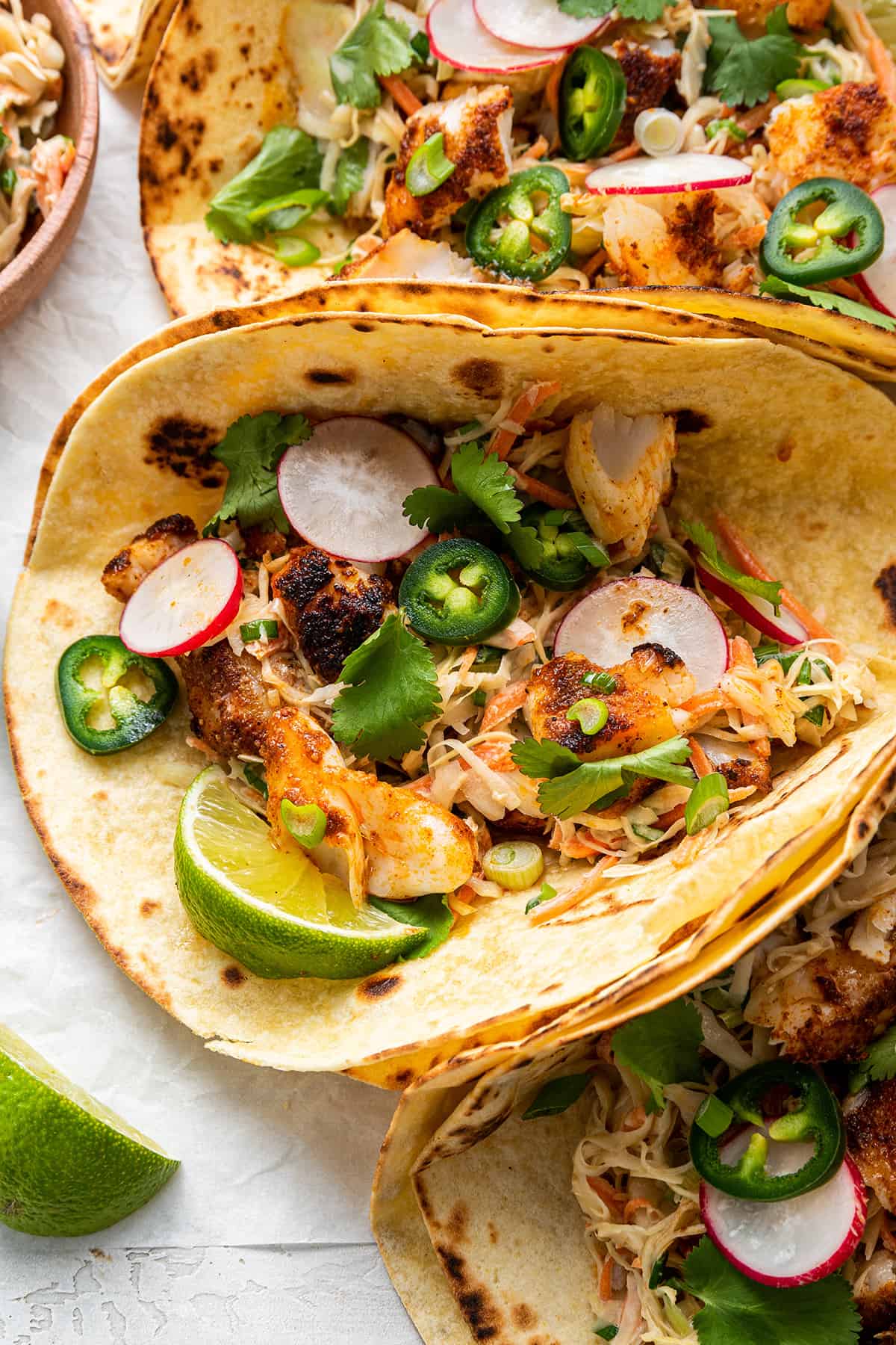 Close up of a folded fish taco topped with lime, jalapeño, and radishes