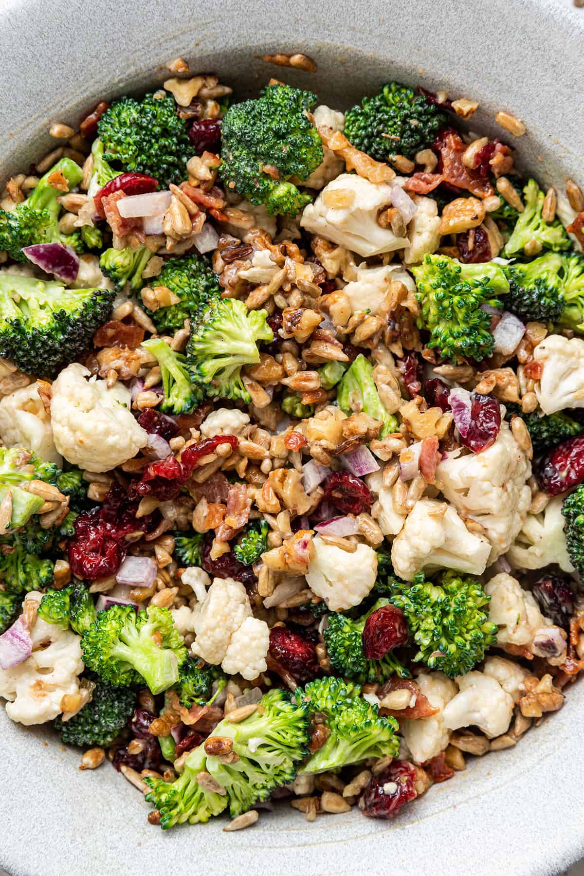 Close up overhead view of a broccoli cauliflower salad with nuts, bacon, and dried cranberries