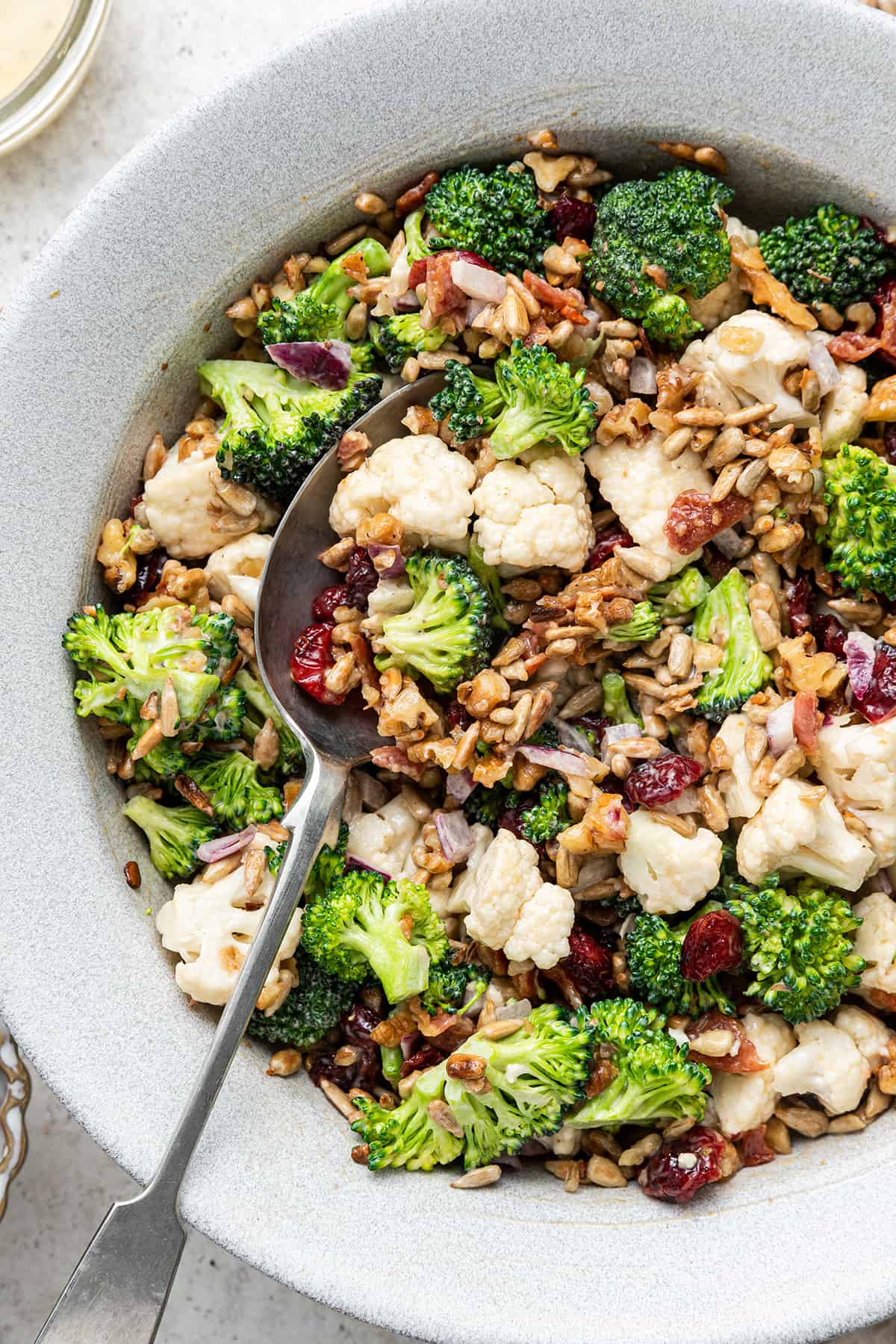Close up overhead of a bowl of broccoli cauliflower salad, with a spoon taking a bite out