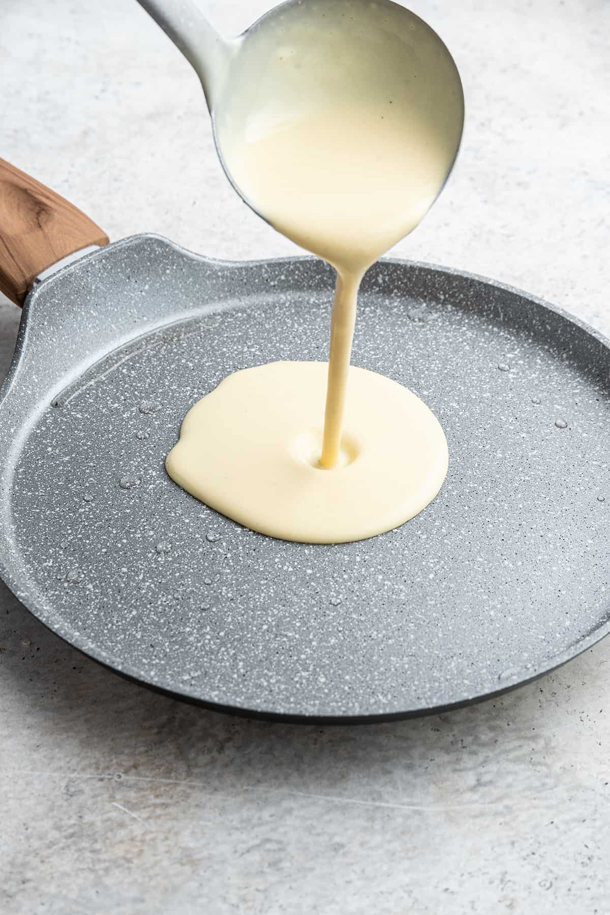 A ladle pouring crepe batter into a pan