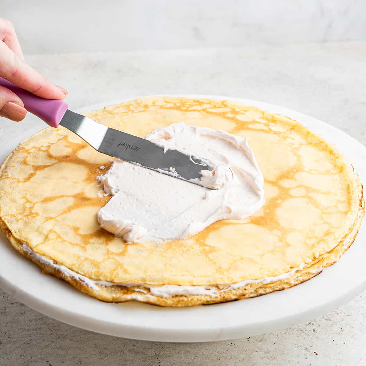 A hand using an offset spatula to spread filling onto a crepe