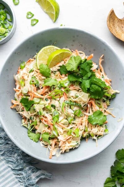 Overhead view of a slaw topped with cilantro and limes, next to a bowl of scallions, a lime slice, and a wooden spoon