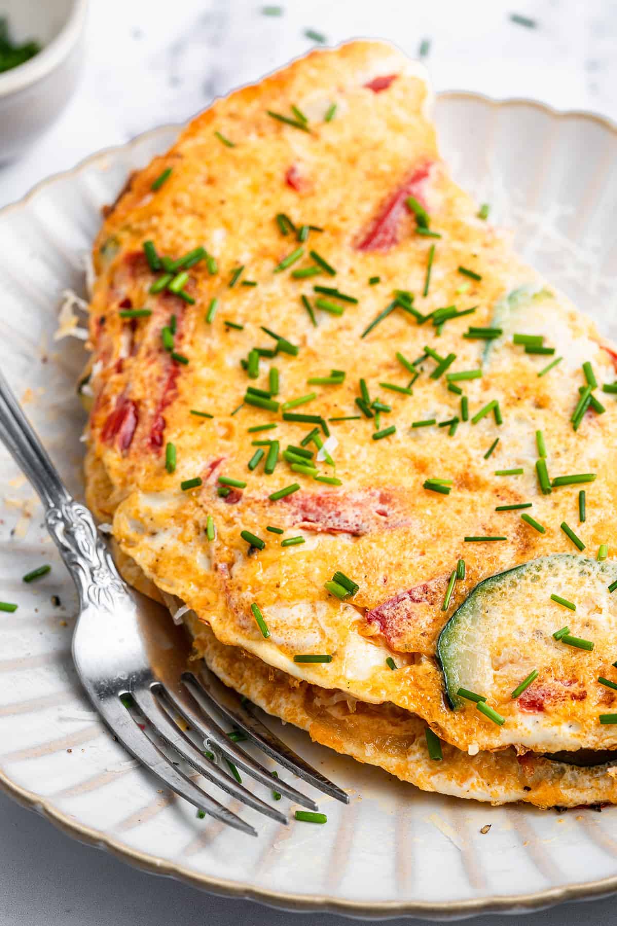 Close up of a veggie omelet on a plate, next to a fork.