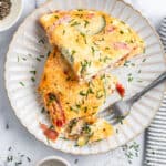 Overhead view of an omelet on a plate, cut in half, with a fork taking a bite from one of the pieces