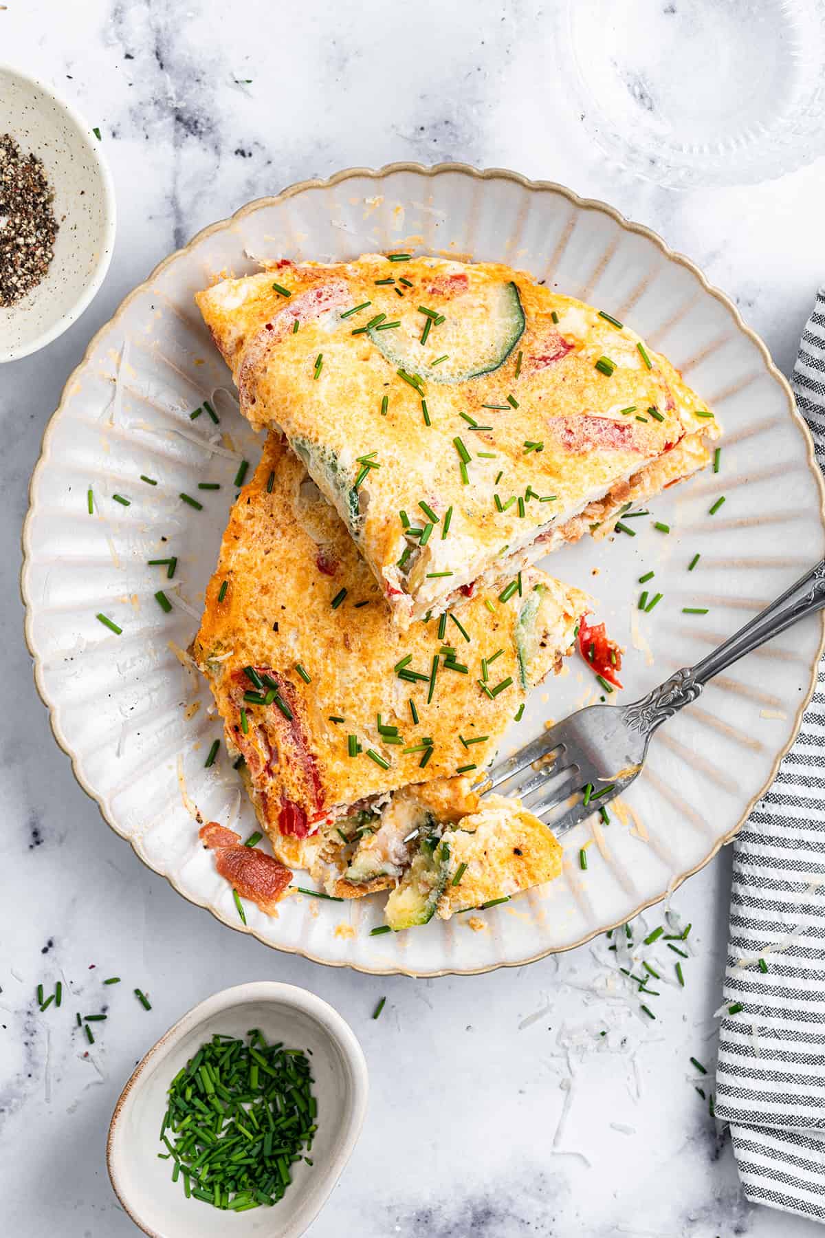 Overhead view of an omelet on a plate, cut in half, with a fork taking a bite from one of the pieces