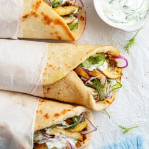 Overhead view of 3 chicken shawarma gyros with small bowl of tzatziki