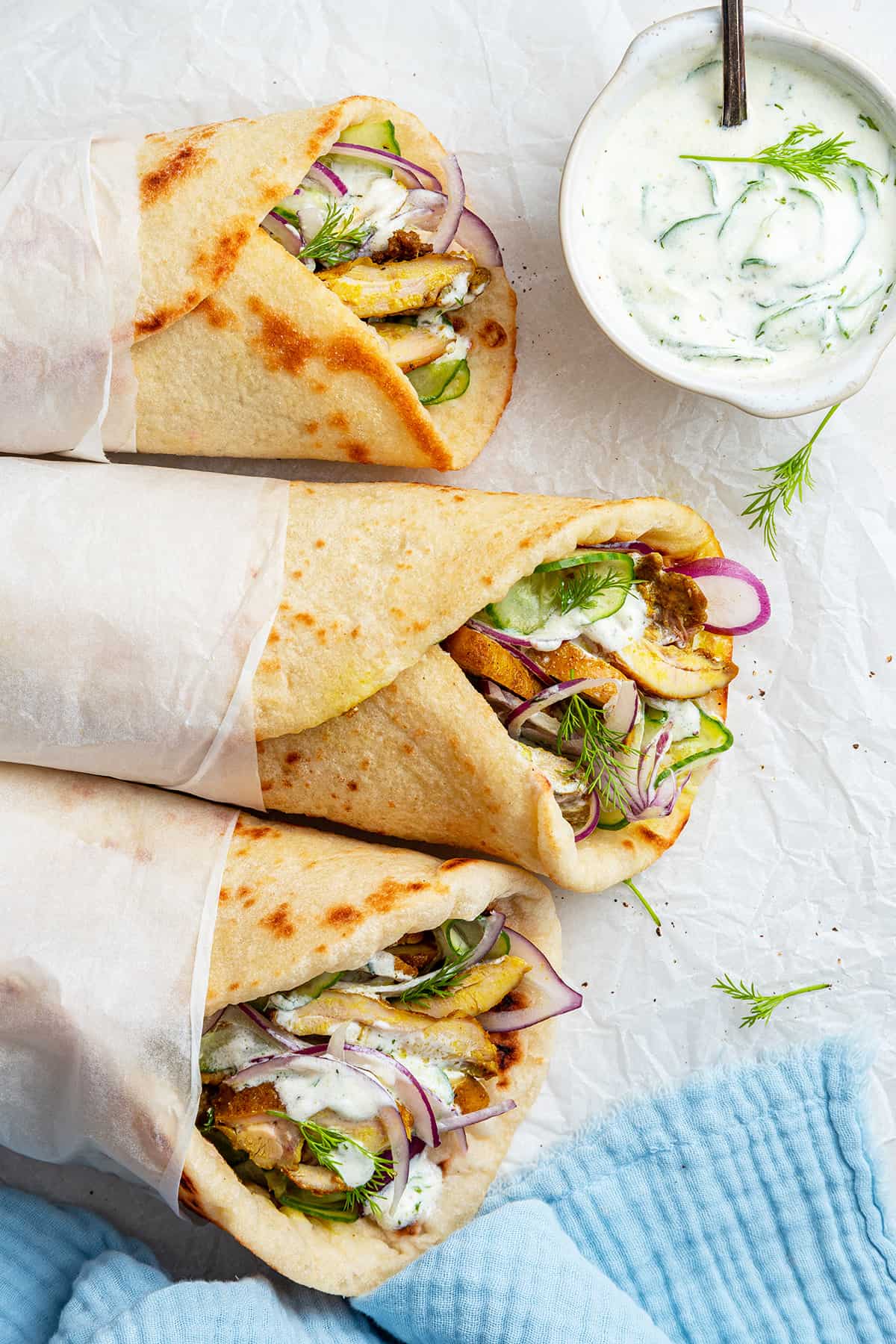 Overhead view of 3 chicken shawarma gyros with small bowl of tzatziki