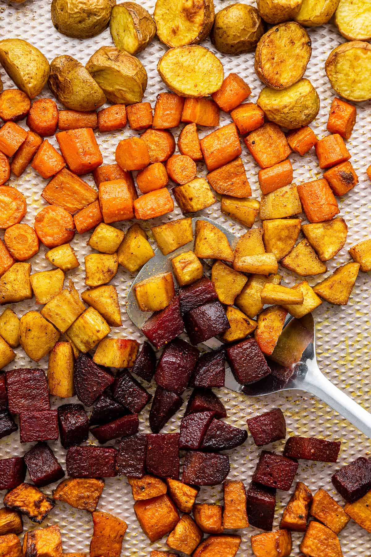 Spatula scooping roasted root vegetables from baking sheet