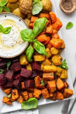 Overhead view of oven-roasted root vegetables on platter with bowl of yogurt dip