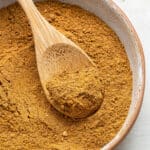 A bowl of ras el hanout with a wooden spoon in it, holding a spoonful of the mixture