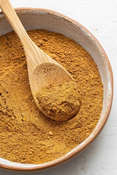 A bowl of ras el hanout with a wooden spoon in it, holding a spoonful of the mixture