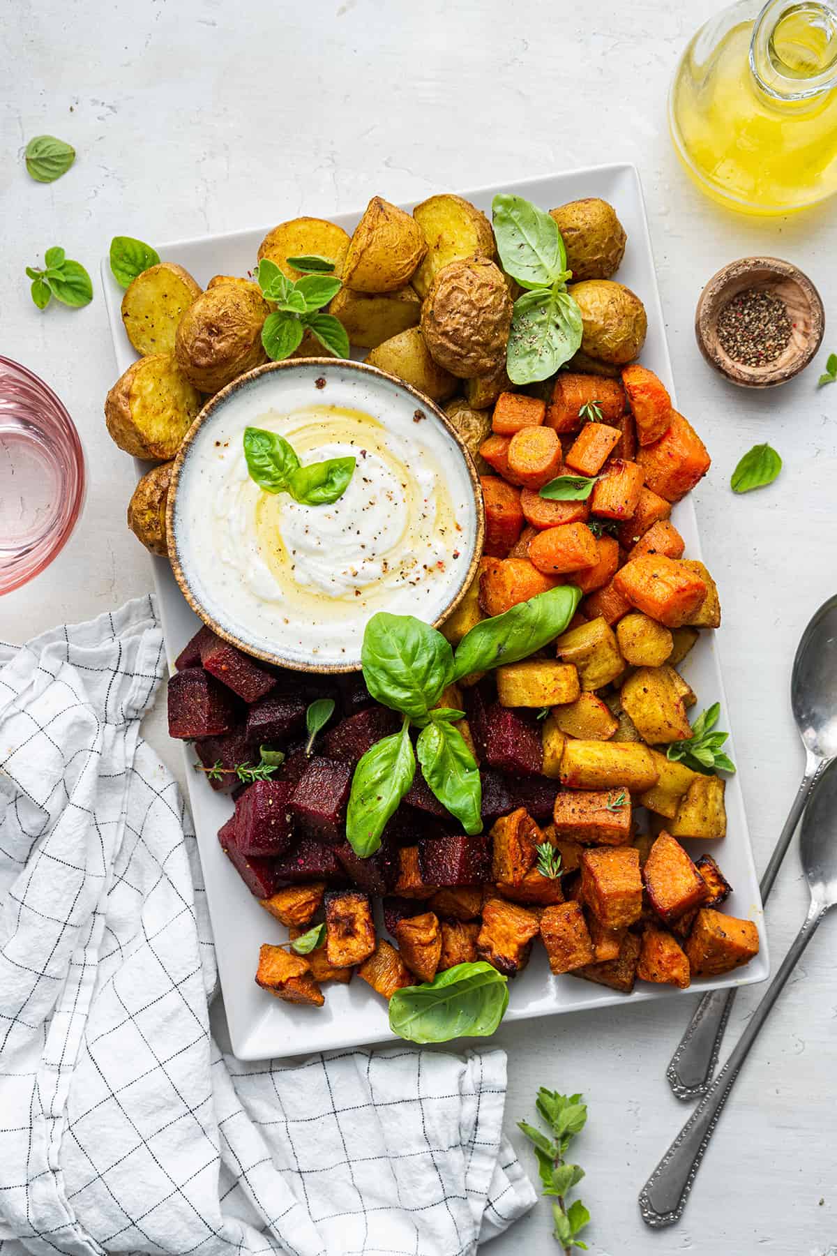Overhead view of yogurt dip on platter with roasted root vegetables and fresh herbs