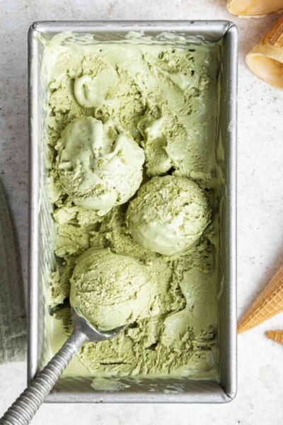 Overhead view of a loaf pan filled with matcha ice cream, with an ice cream scoop scooping a ball of ice cream