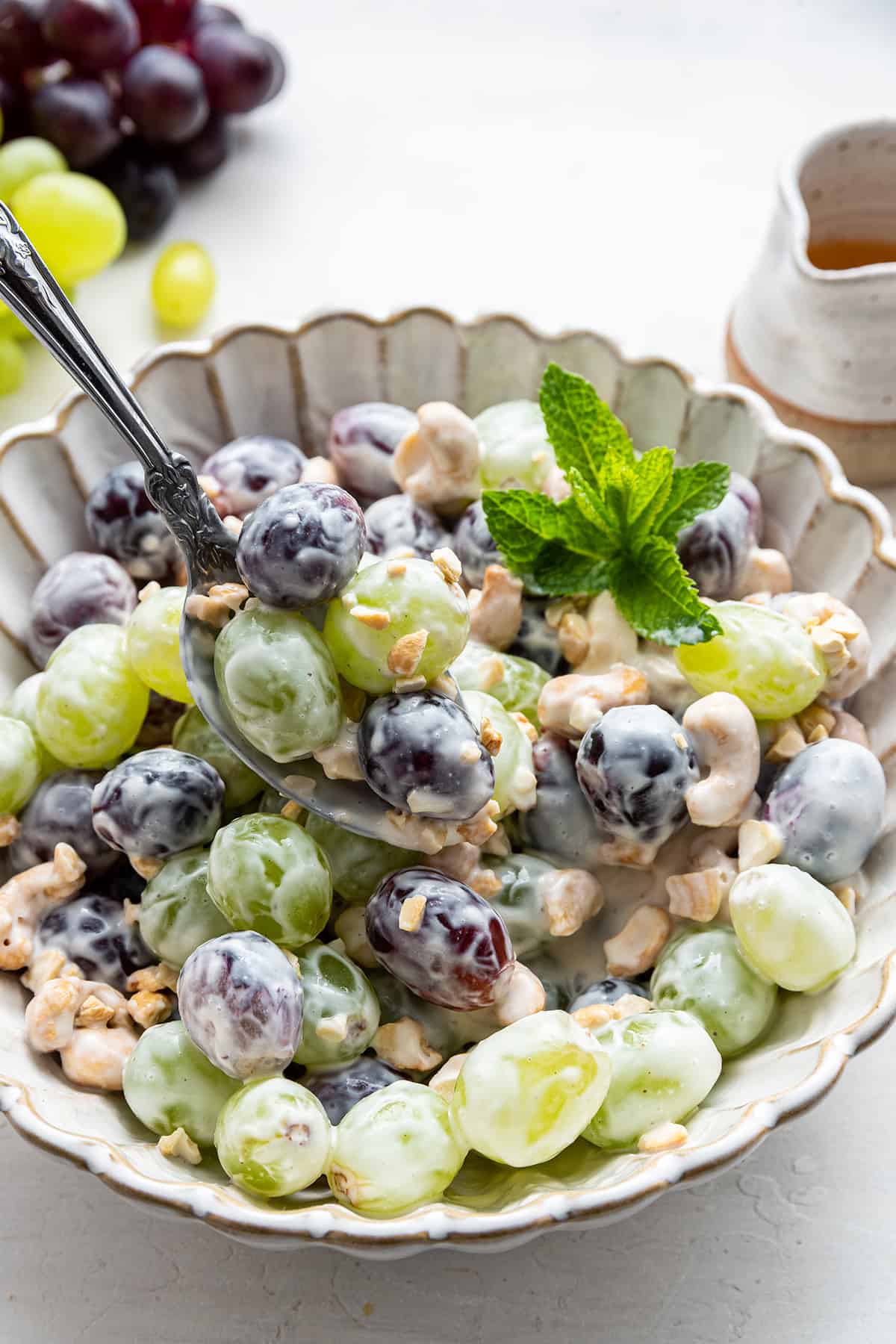 A bowl of grape and yogurt salad with a spoon taking a spoonful out