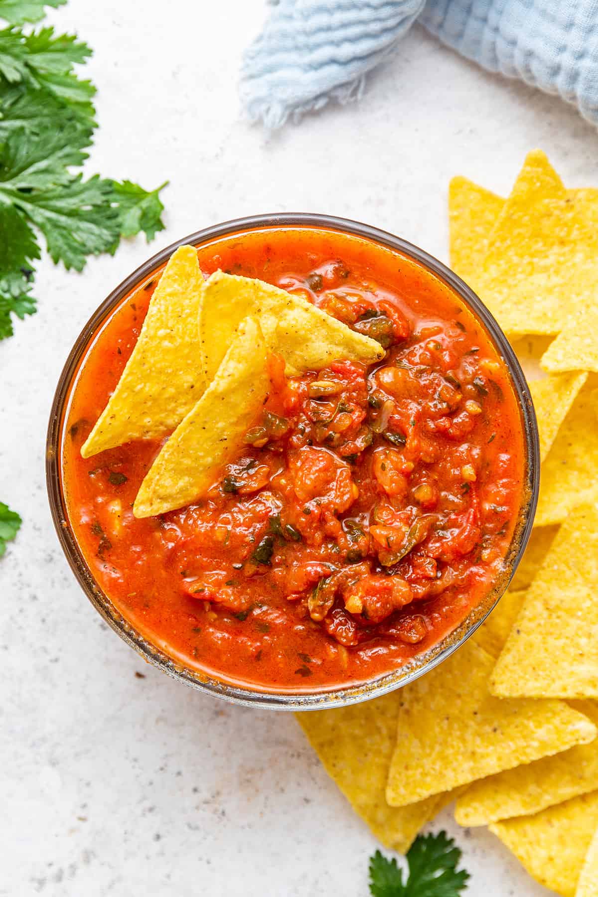 Three tortilla chips in bowl of salsa roja, with additional chips on the side