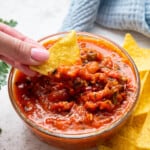 Hand dipping tortilla chip into salsa roja