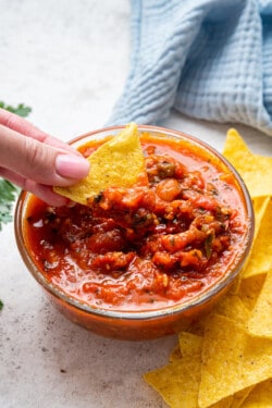 Hand dipping tortilla chip into salsa roja