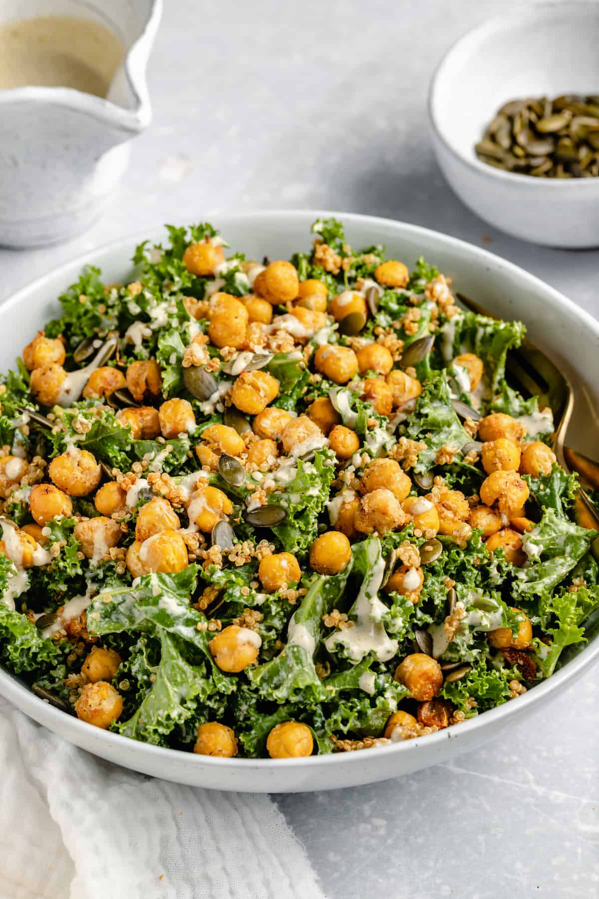 Vegan kale Caesar salad in a white bowl topped with crispy chickpeas and tahini dressing.