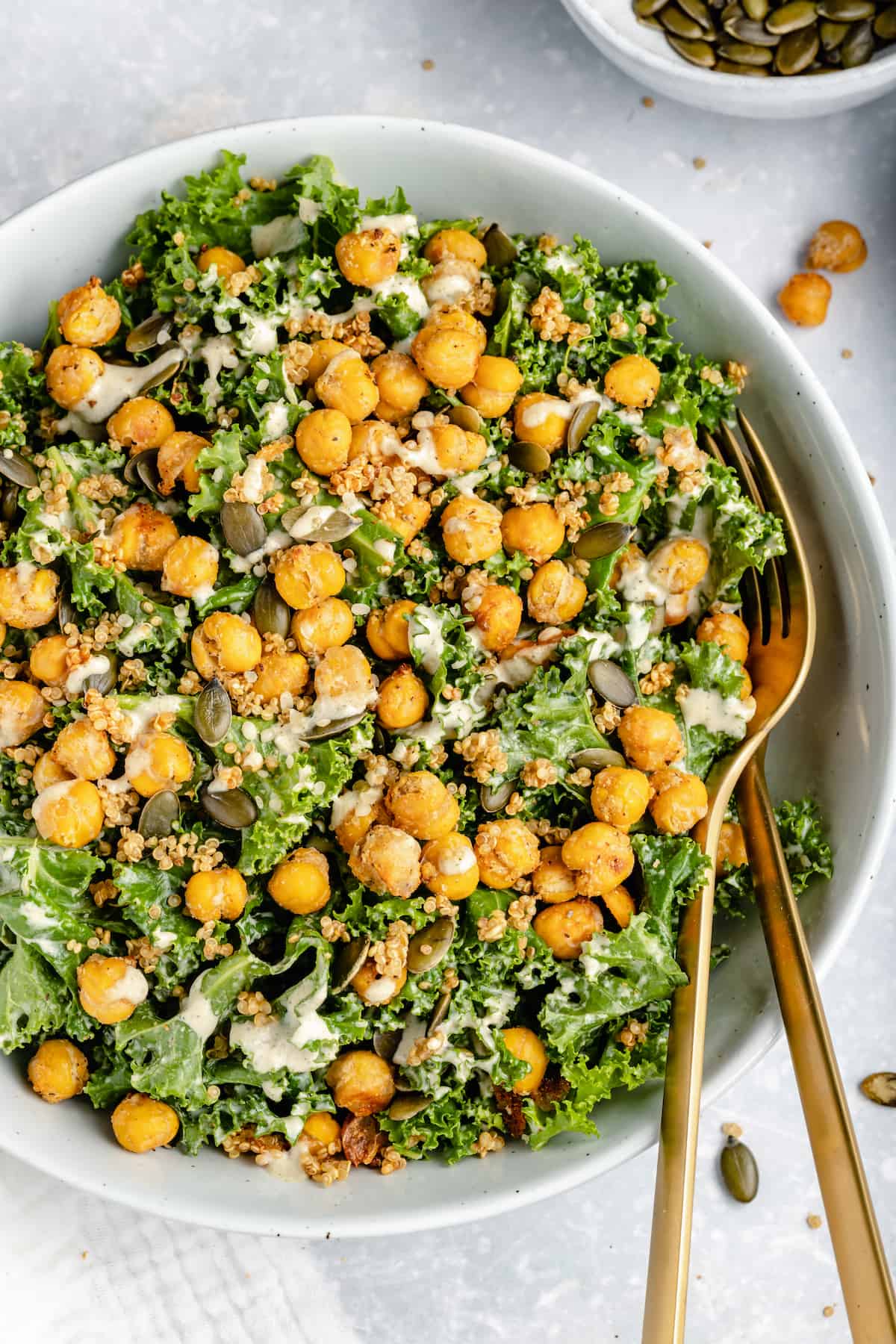 Overhead view of vegan kale Caesar salad in a white bowl topped with crispy chickpeas and tahini dressing.