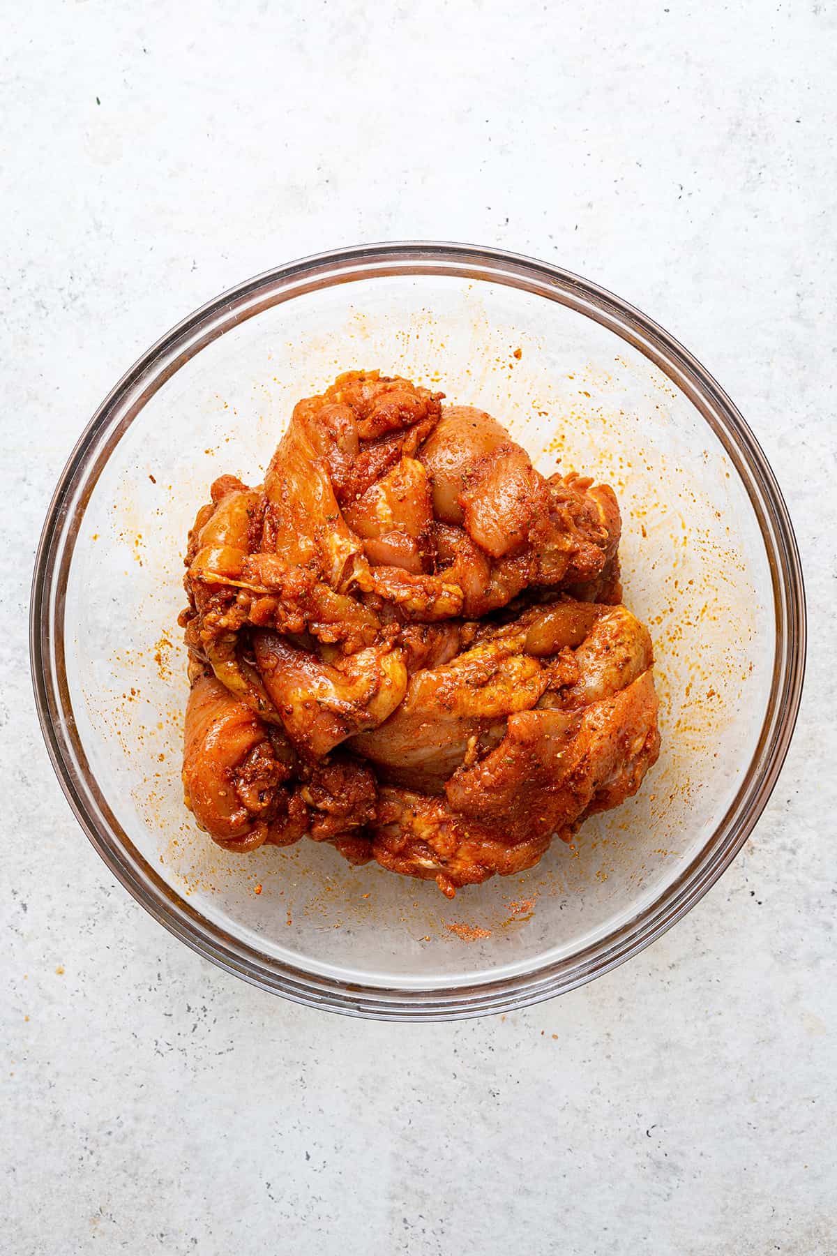 Overhead view of chicken thighs in glass bowl with blackened seasoning