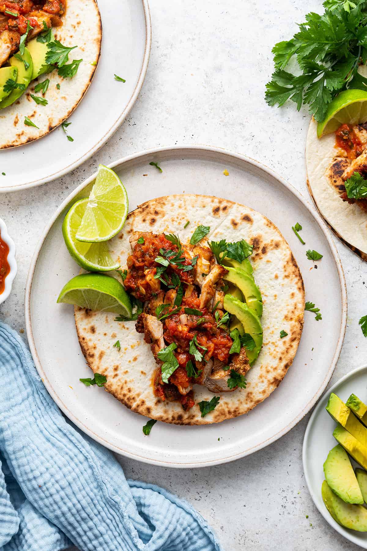 Overhead view of open blackened chicken taco on plate with salsa, sliced avocado, and lime