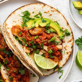 Overhead view of two blackened chicken tacos on a plate, garnished with cilantro, lime wedge, and avocado slices