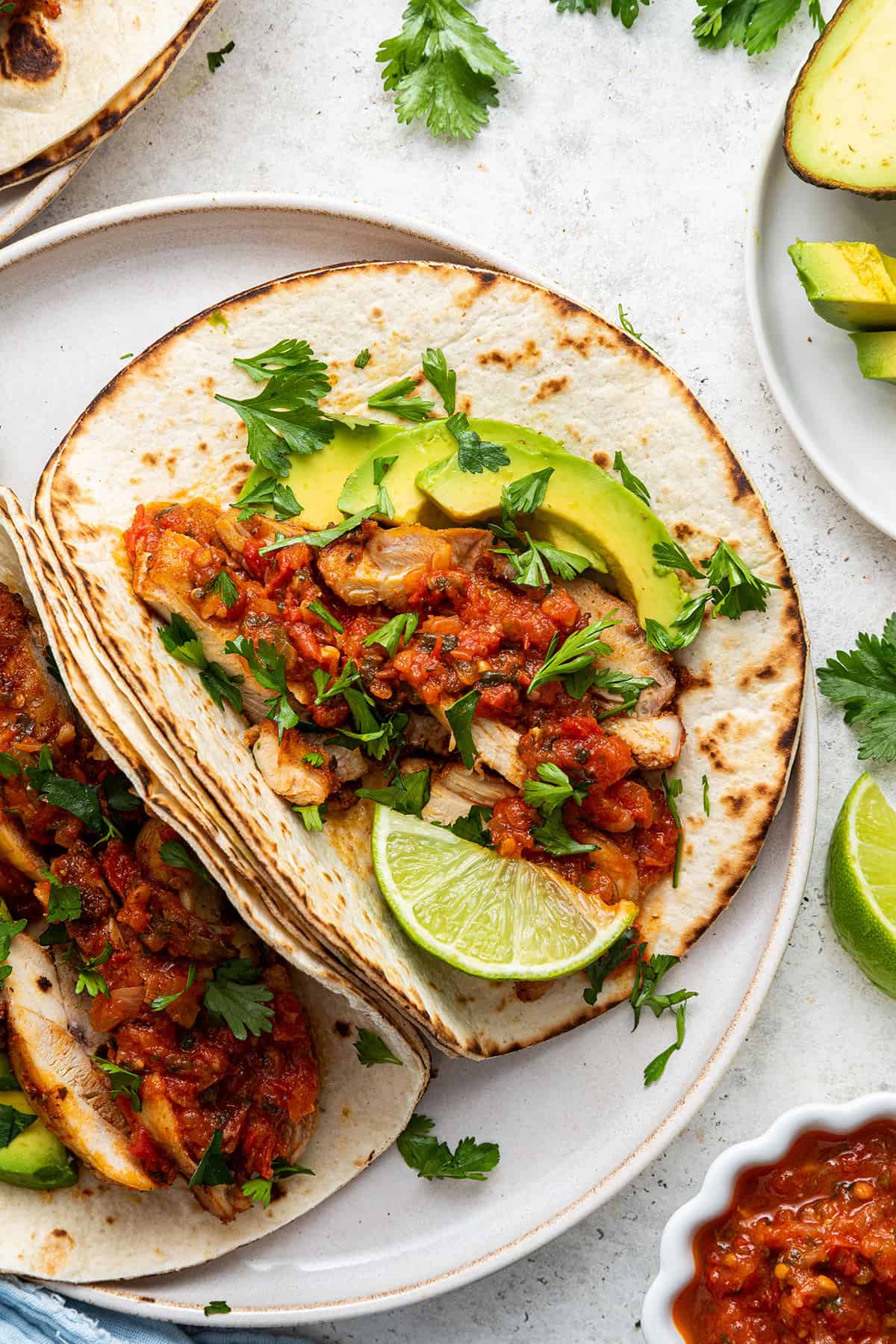 Overhead view of two blackened chicken tacos on a plate, garnished with cilantro, lime wedge, and avocado slices