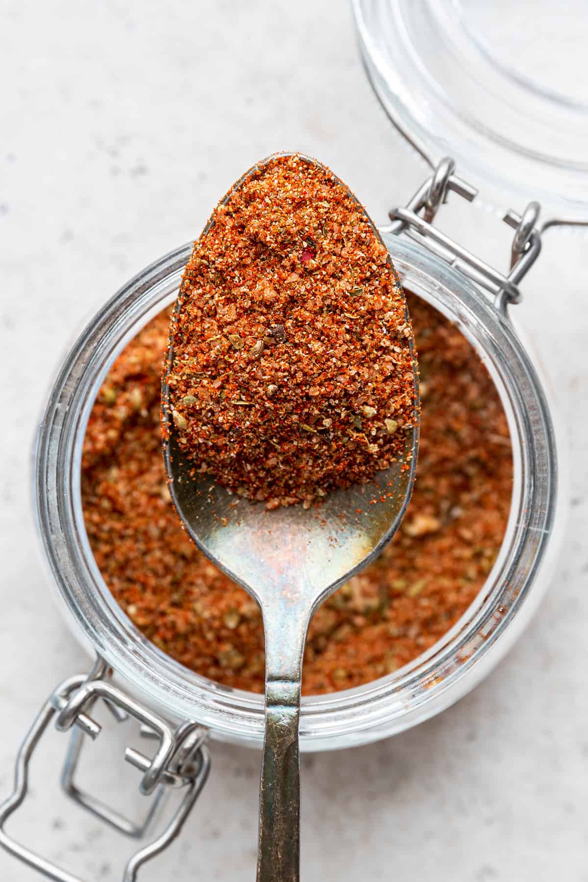 Closeup of blackened seasoning in spoon held over open jar