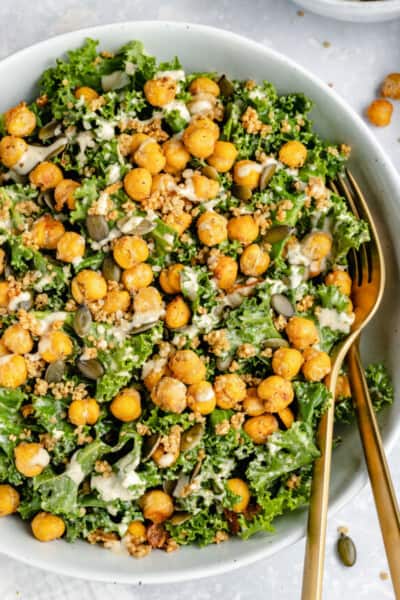 Overhead view of vegan kale Caesar salad in a white bowl topped with crispy chickpeas and tahini dressing.