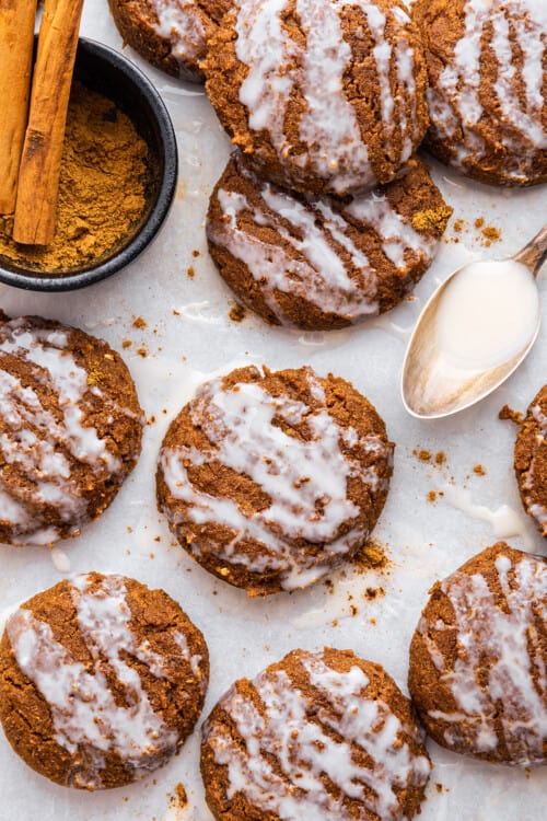 Overhead view of frosted pumpkin cookies on parchment paper with spoonful of coconut butter and bowl of cinnamon