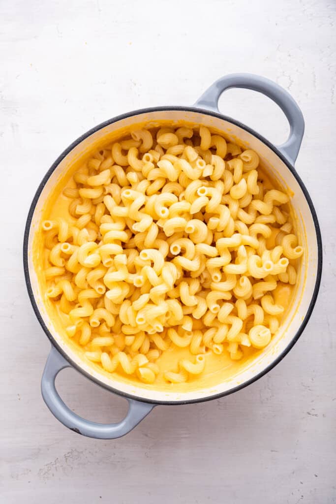 Overhead view of pasta added to cheese sauce in Dutch oven