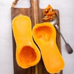 Overhead view of halved butternut squash on cutting board with spoonful of seeds