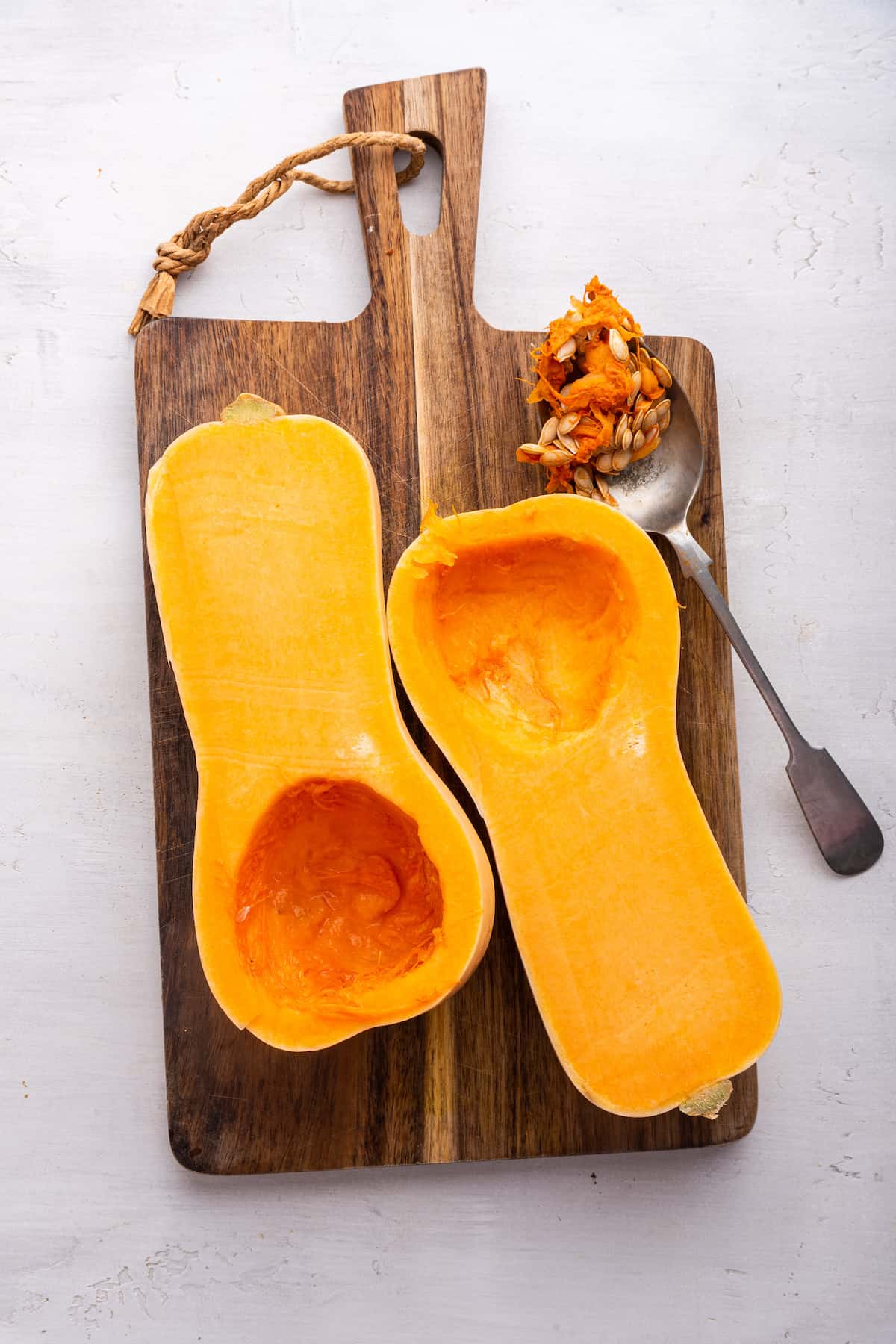 Overhead view of halved butternut squash on cutting board with spoonful of seeds