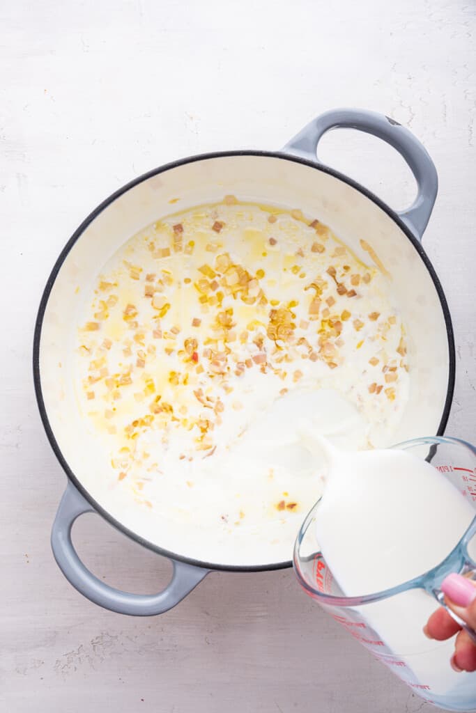 Pouring milk into Dutch oven with cooked shallots and garlic