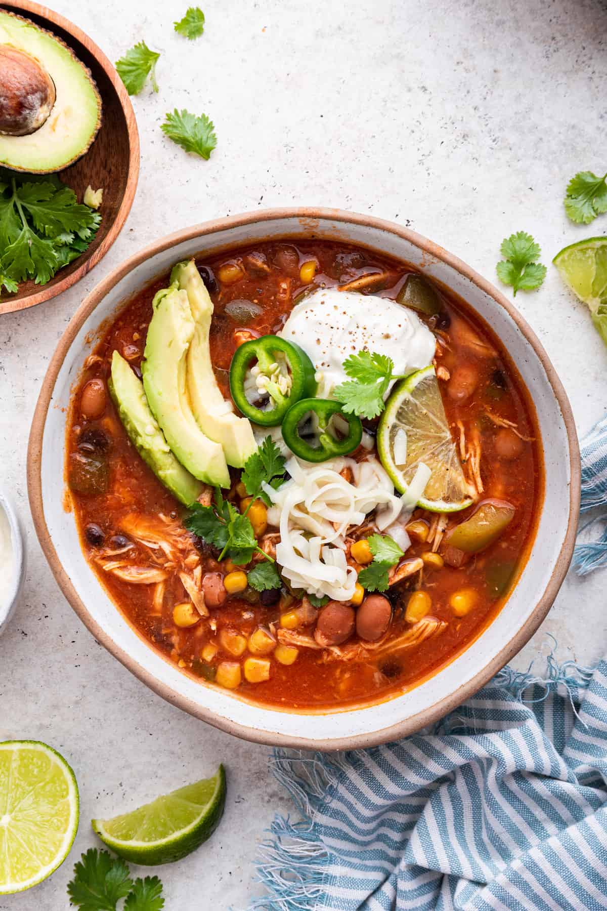 Overhead view of crockpot chicken taco soup in bowl with avocado, cheese, sour cream, lime, and cilantro