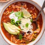 Overhead view of taco soup in bowl, garnished with avocado, cilantro, cheese, sour cream, and lime