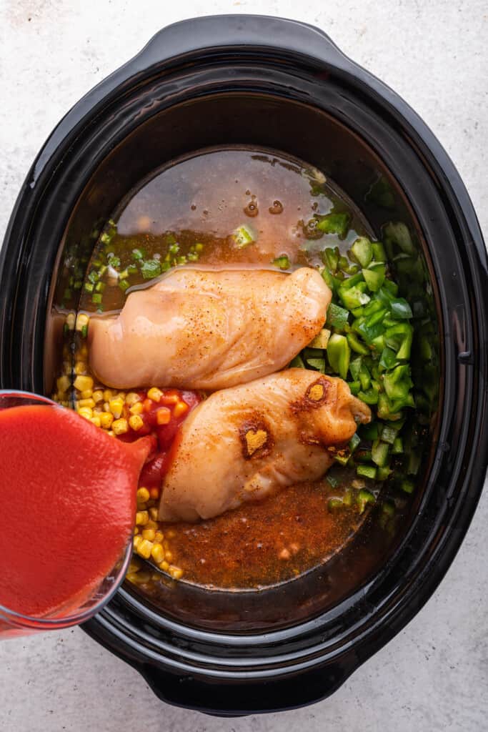 Overhead view of tomato sauce being poured into slow cooker insert with other soup ingredients