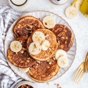 Overhead view of oatmeal banana pancakes on plate with pecans and bananas