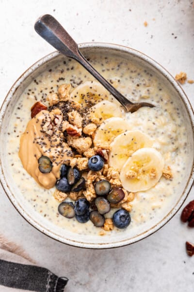 Overhead view of spoon in bowl of creamy protein oatmeal with toppings