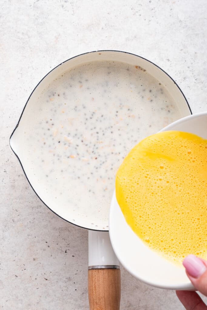 Overhead view of beaten eggs being poured into saucepan for protein oatmeal