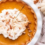 Overhead view of sliced pumpkin pie topped with whipped cream, cinnamon, and nuts