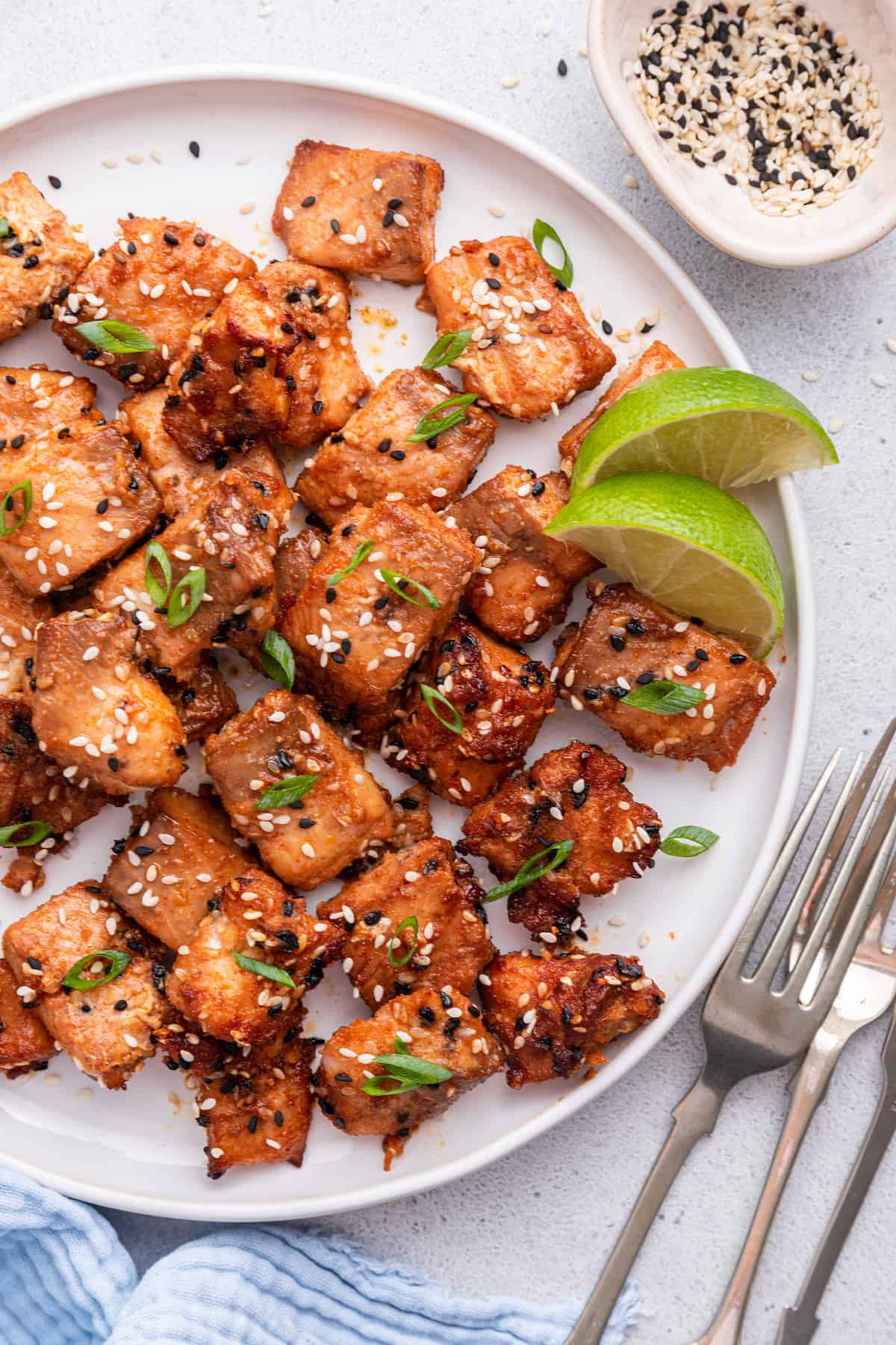 Overhead view of air fryer salmon bites on plate with lime wedges