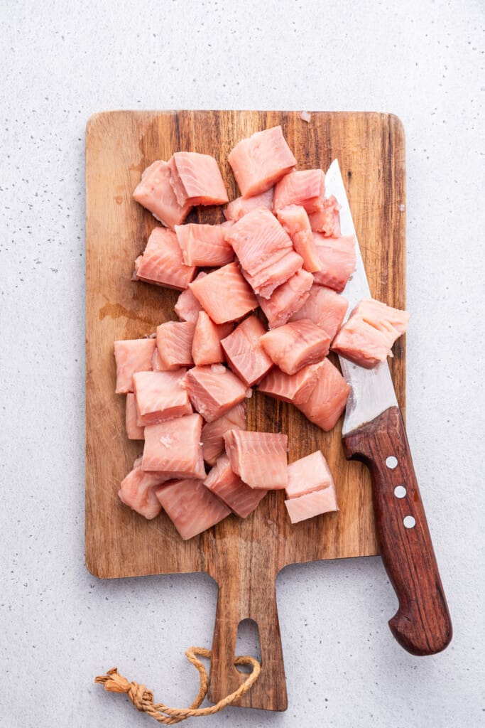 Overhead view of salmon cut into bite-sized pieces on cutting board with knife