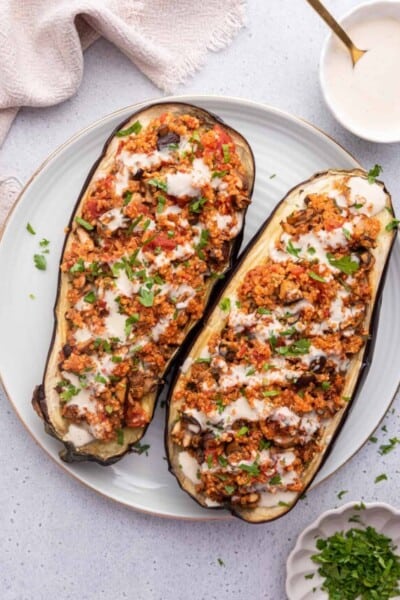 Overhead view of stuffed eggplant on plate next to bowls of tahini and parsley