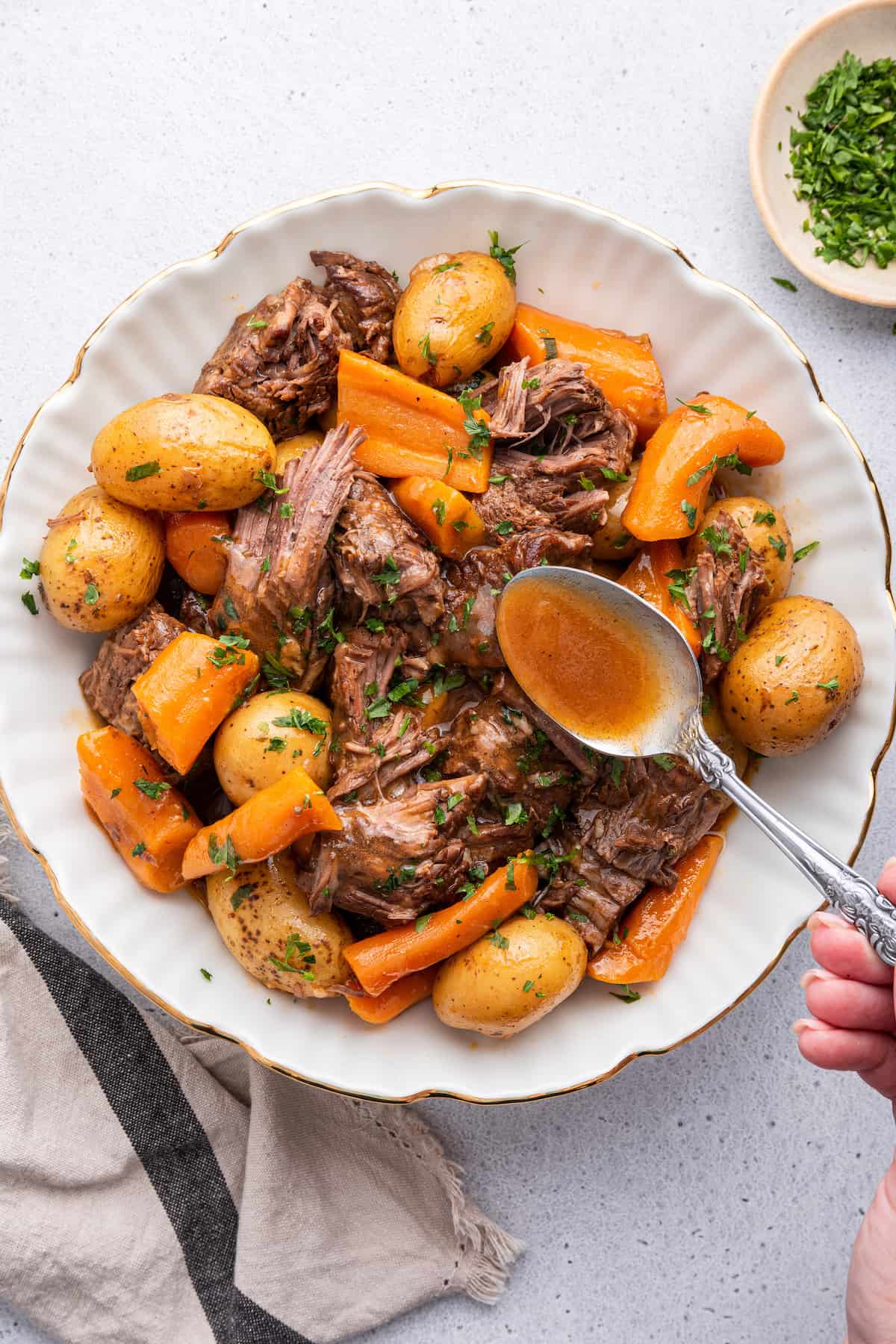Overhead view of spoon drizzling gravy onto serving bowl of Instant Pot chuck roast with potatoes and carrots