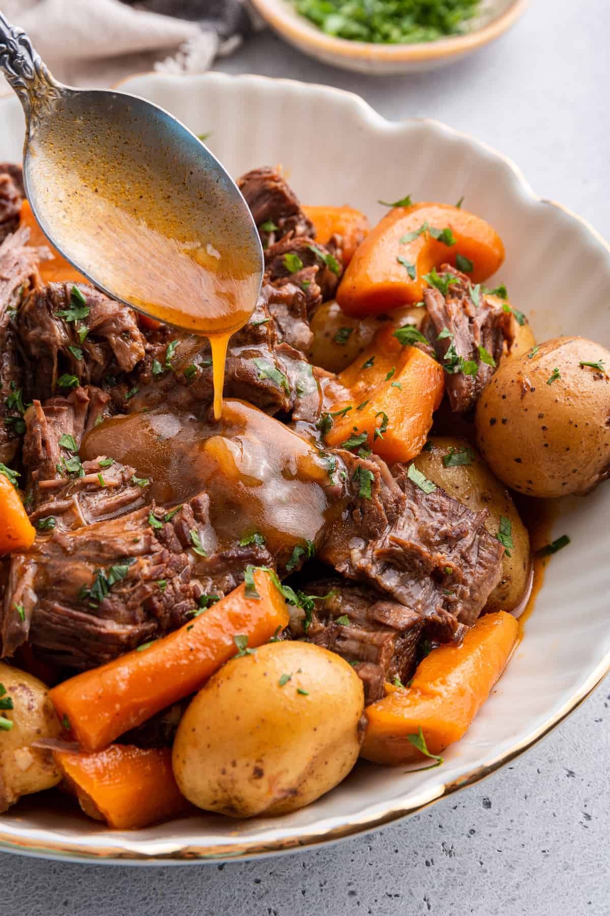 Spoon drizzling gravy onto Instant Pot chuck roast in serving bowl