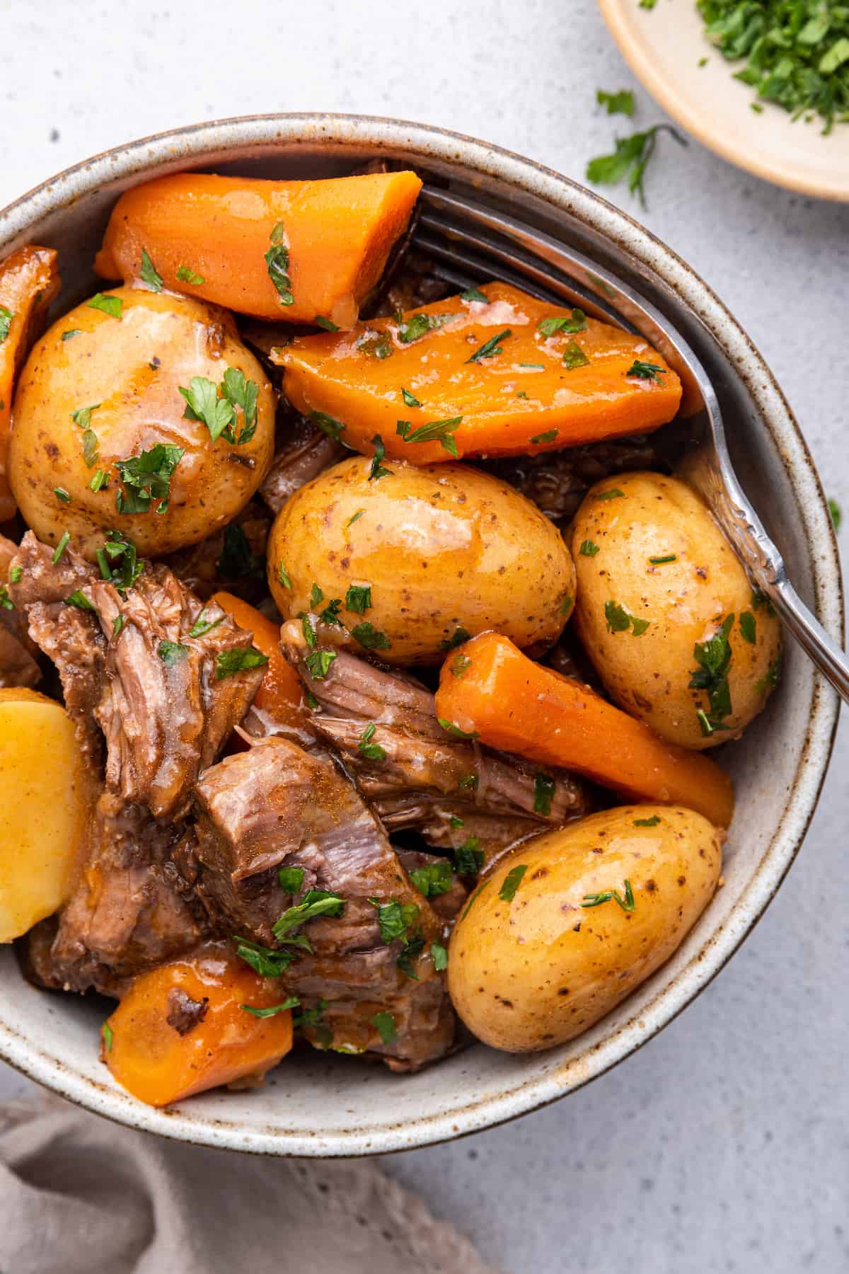 Overhead view of Instant Pot chuck roast with potatoes and carrots in bowl with fork
