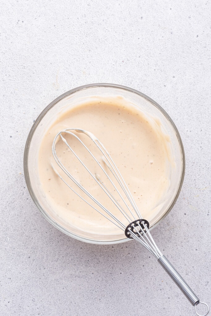 Overhead view of tahini sauce in glass bowl with whisk